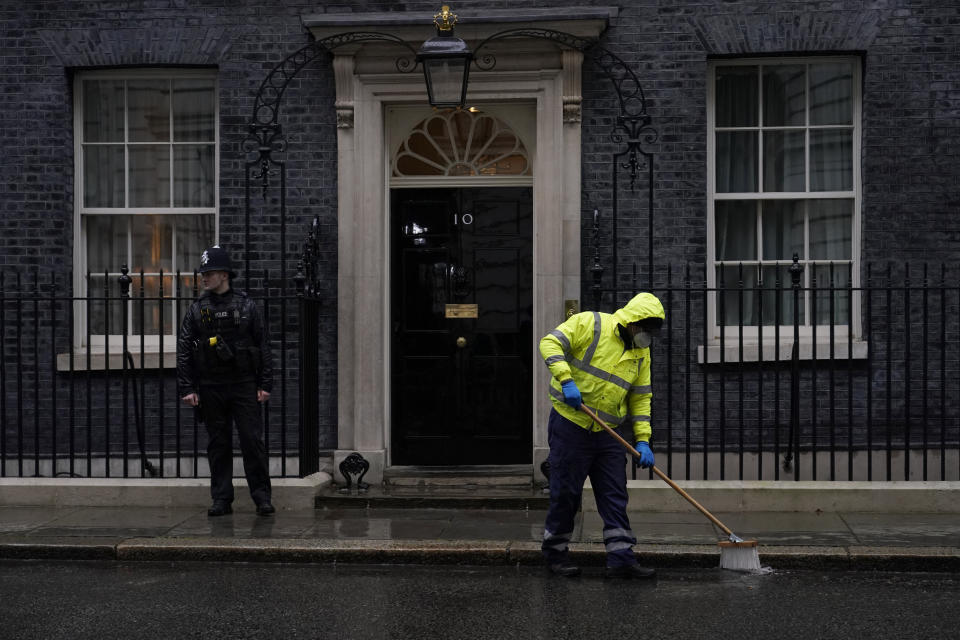 A worker sweeps in the rain and a police officer stands guard outside the door of 10 Downing Street, in London, Friday, Feb. 4, 2022. Four of Boris Johnson's most senior staff quit on Thursday, with a fifth staff member resigning on Friday morning, triggering new turmoil for the embattled British prime minister. Johnson's grip on power has been shaken by revelations that his staff held "bring your own booze" office parties, birthday celebrations and "wine time Fridays" in 2020 and 2021 while millions in Britain were barred from meeting with friends and family during coronavirus lockdowns. (AP Photo/Alberto Pezzali)