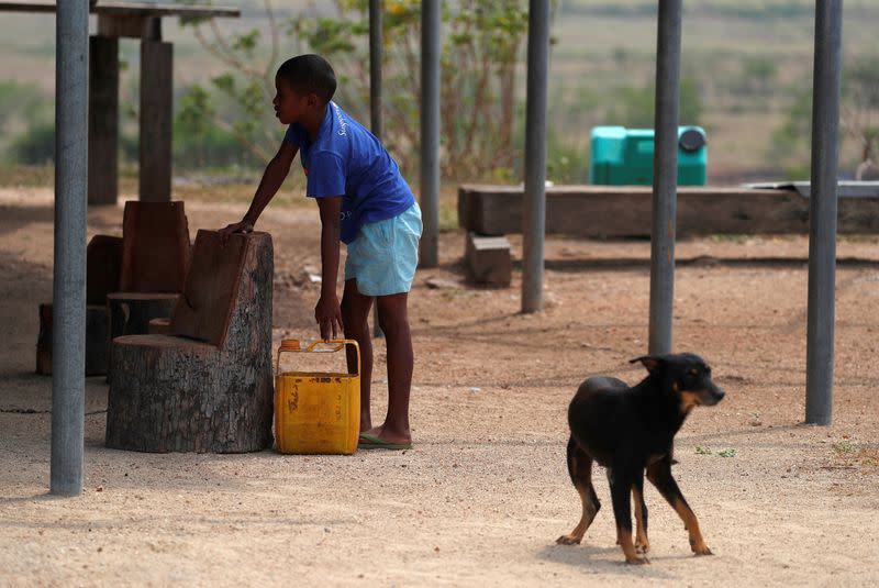 FILE PHOTO: A dog stands near a boy as he prepares to carry a container to collect water as he stands under his house in the village of Papa Lea Lea on the outskirts of Port Moresby