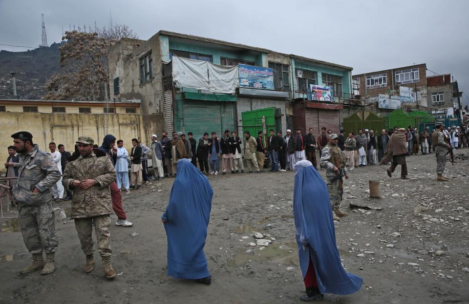 Afghan men line up for registration process before they cast their votes outside a polling station as burqa-clad women walk past the polling station in Kabul, Afghanistan, Saturday, April 5, 2014. The Taliban threatened to target voters and polling places, but there were few instances of violence. Instead, those wanting to cast ballots joined long lines and expressed pride for security forces guarding the election and a willingness to stand up for their country. (AP Photo/Massoud Hossaini)