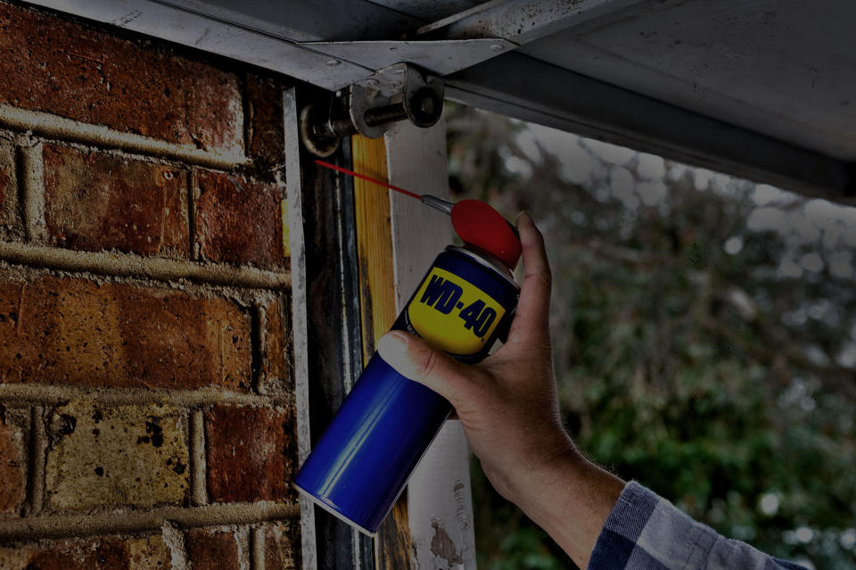 A man's hand using a can of WD-40 in a garage.