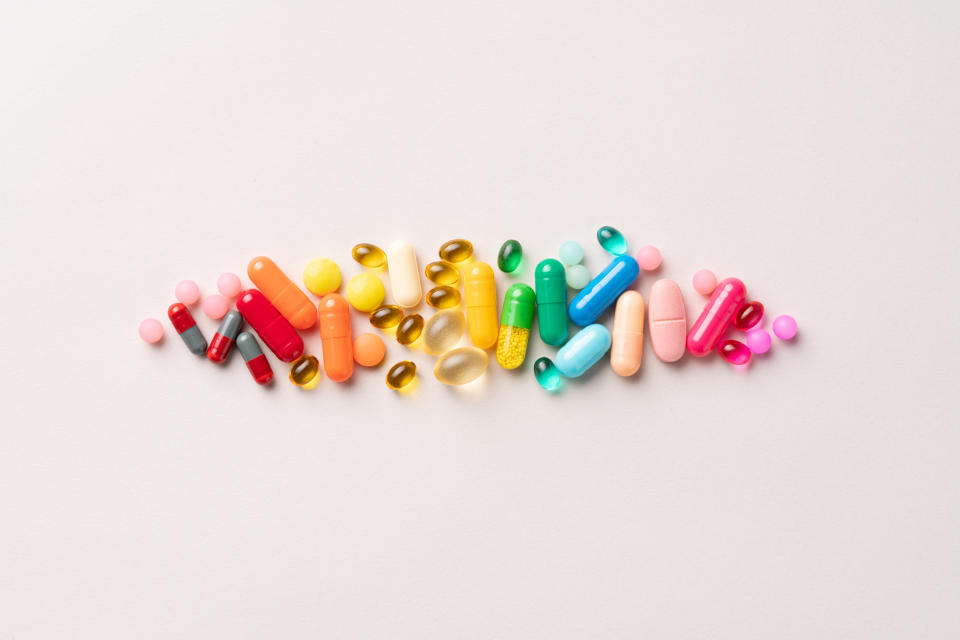 A variety of pills and capsules of different shapes and sizes are arranged in a row on a plain background, depicting various types of medication