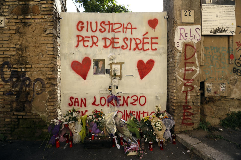 Flowers lie by a writing on a door reading in Italian "Justice for Desiree", outside the abandoned building where a 16-year-old girl was murdered, in Rome, Thursday, Oct. 25, 2018. Italian police have detained three suspects, all immigrants, in the slaying of a teenage girl who was drugged, gang-raped and left in an abandoned building known as a center for drug dealing in Rome. Authorities said Thursday that the three suspects, two Senegalese citizens and one Nigerian, were being held on suspicion of murder, group sexual assault and handing out drugs in the death late last week of 16-year-old Desiree Mariottini. (AP Photo/Gregorio Borgia)