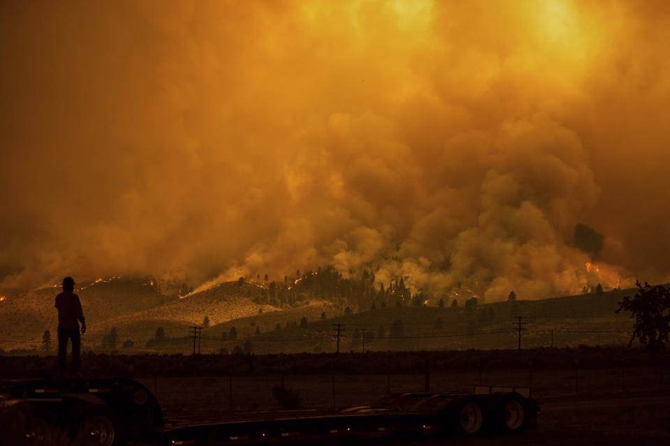 A man's silhouette in the foreground of a whole hillside consumed in smoke