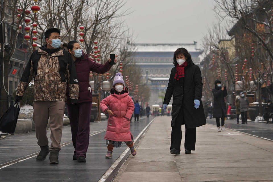 Family members wearing face masks to help protect from the coronavirus tour Qianmen Street, a popular tourist spot in Beijing, Sunday, Jan. 23, 2022. Chinese authorities have called on the public to stay where they are during the Lunar New Year instead of traveling to their hometowns for the year's most important family holiday. (AP Photo/Andy Wong)