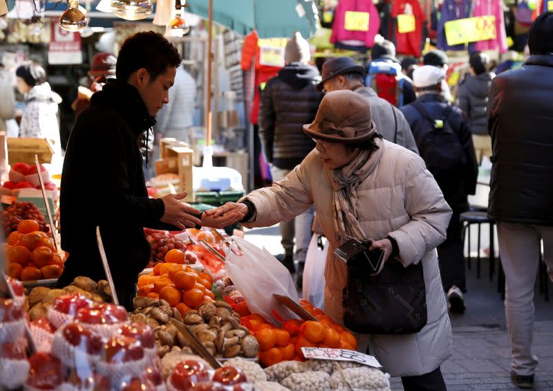 FILE PHOTO: A woman pays money as she buys fruits outside a vegetable store at Ameyoko shopping district in Tokyo