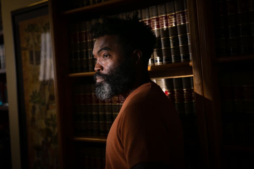 Damien Smith poses for a portrait in a lawyer's office, standing near a bookshelf