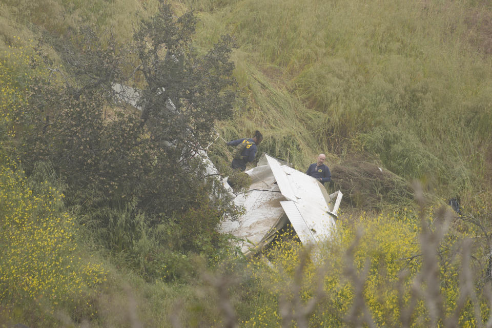 National Transportation Safety Board investigators inspect a downed plane on a steep hill covered with fog above a home on Beverly Glen Circle in Los Angeles, Sunday, April 30, 2023. Fire department officials said a person was found dead following an intensive search for the single-engine airplane that crashed in a foggy area Saturday night. (AP Photo/Damian Dovarganes)