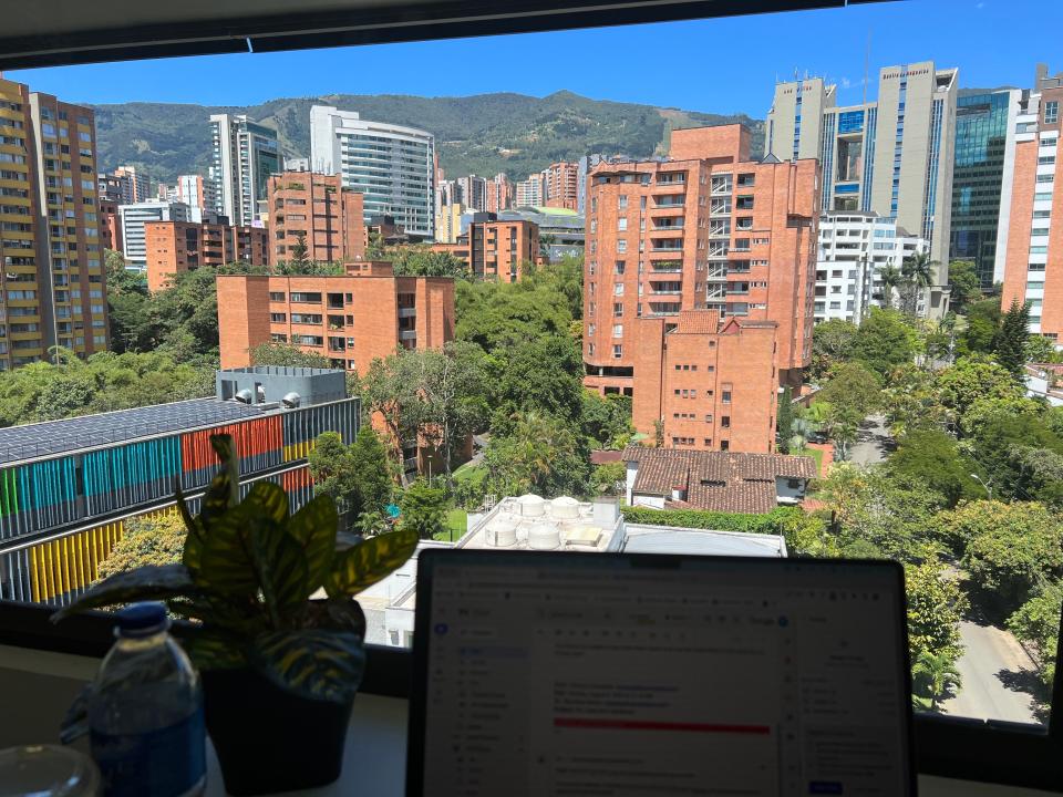 A desk with a computer and a view of a city behind it.