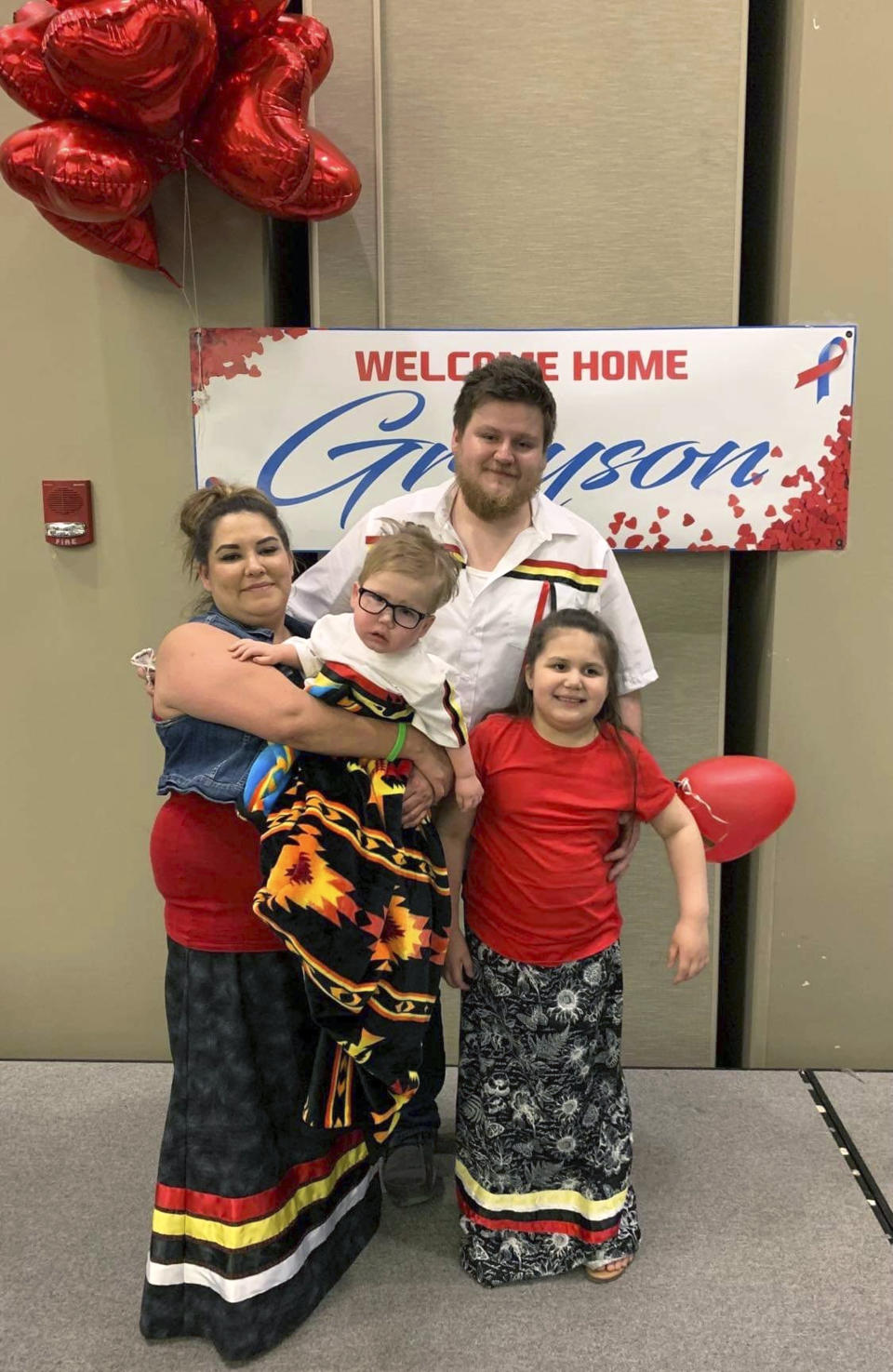 In this photo provided by Joan Azure, Azure's grandson Greyson Parisien, center, is held by mother, Reeanne, while posing for a photo with dad, Ridge Parisien, and sister, Parker, after Greyson returned home to Belcourt, N.D, in July 2019, after a heart transplant. Greyson's journey to correct a heart defect led the Turtle Mountain Band of Chippewa Indians to designate a spot on tribal IDs for organ donation. (Joan Azure via AP)