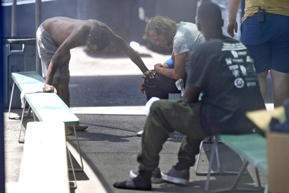 People keep cool under misters outside a homeless shelter, Thursday, May 30, 2024 in Phoenix. Sizzling sidewalks and unshaded playgrounds increasingly are posing risks for surface burns as air temperatures reach new highs during the searing summers in Southwest cities like Phoenix and Las Vegas. Very young children and older adults are especially at risk for contact burns. So are homeless people. (AP Photo/Matt York)