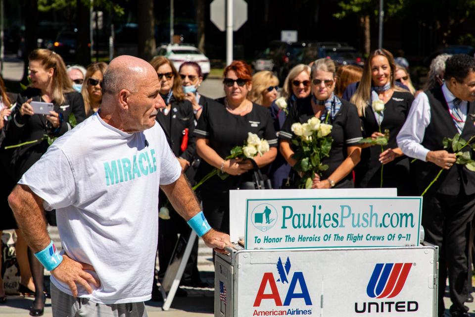 Paulie Veneto, of Braintree, is trailed by United Airlines flight attendants as he stops to look at the 9/11 Memorial at Logan Airport on Saturday, Aug. 21, 2021.