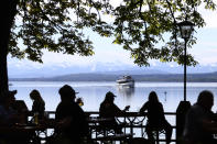 FOR HOLD - In this Monday, May 10, 2021 file photo, people enjoy the sunny weather and drink beer on the re-opening day of beer gardens, following the lifting of measures to avoid the spread of the corona virus, at Bavarian lake 'Ammersee' in front of the alps in Inning, Germany. Germany has overall managed the pandemic far better than many of its peers and its daily death toll remains significantly below that of neighboring France, which has a smaller population, for instance. All three candidates for chancellor have said no further lockdown is planned. (AP Photo/Matthias Schrader, File)