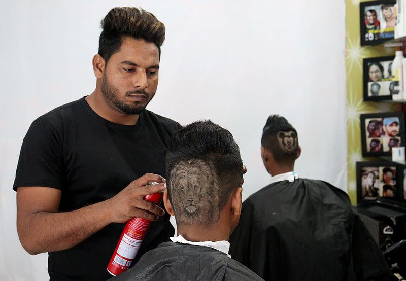 Gurwinder Singh Sidhu gives finishing touches to the hair of a customer after making a hair tattoo in the shape of a lion on his head, in Dabwali