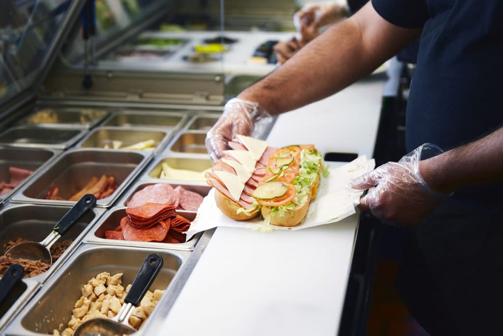 A person makes a sub sandwich in a sub shop. 