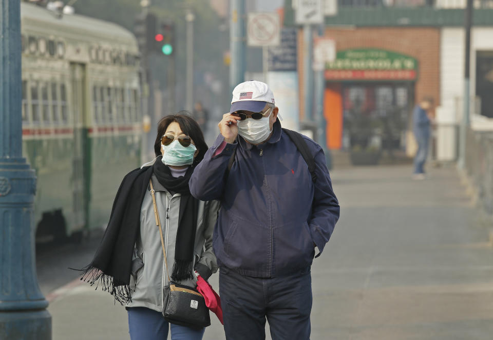 FILE - In this Nov. 16, 2018 file photo, a couple wears masks while walking at Fisherman's Wharf through smoke and haze from wildfires in San Francisco. From air pollution triggered by wildfires that caused people in Northern California to don breathing masks to increased asthma attacks that send children to the hospital, medical experts said climate change is hurting people’s bodies. (AP Photo/Eric Risberg, File)