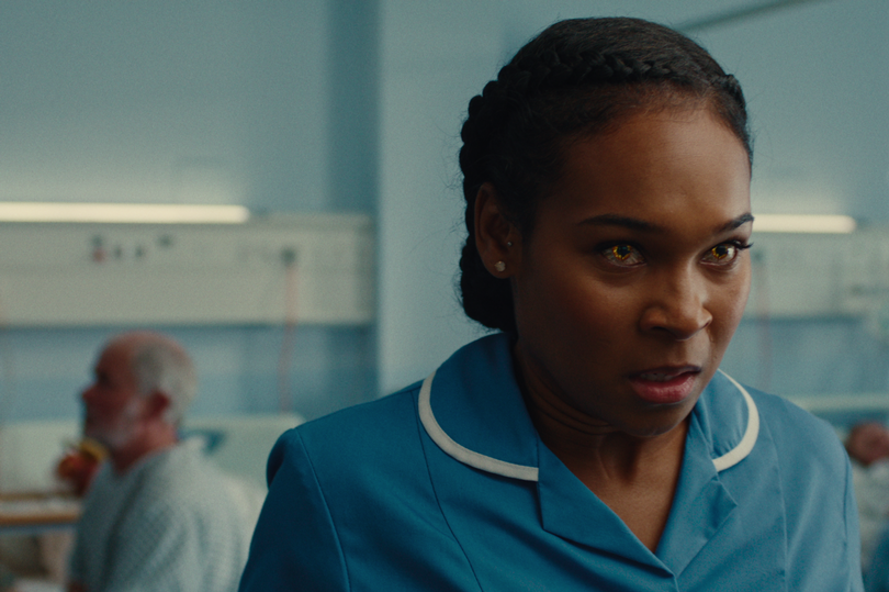 A black woman in a hospital wearing scrubs with a confused facial expression and red eyes