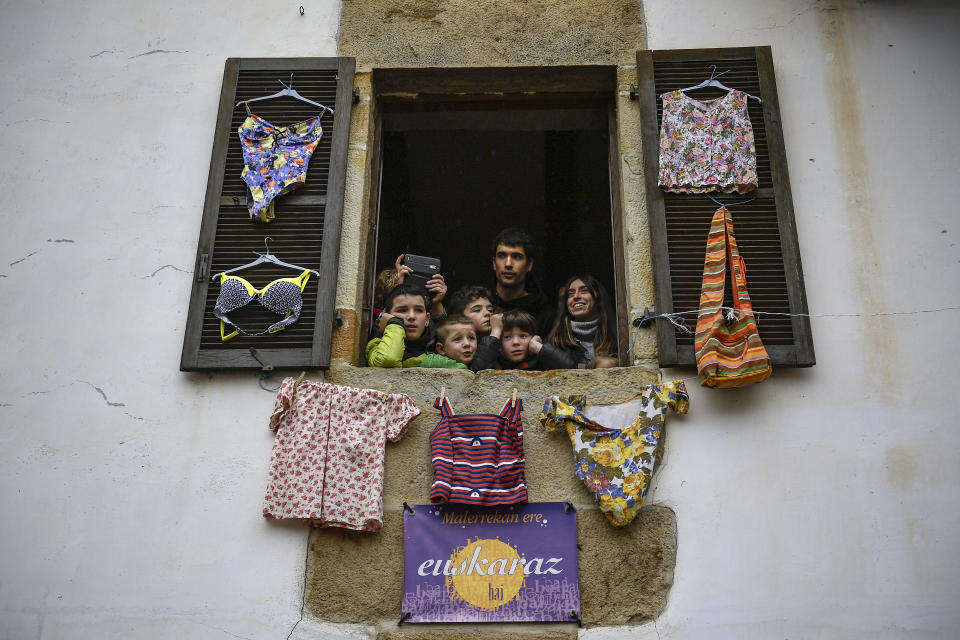 In this Monday, Jan. 27, 2020 photo, residents look from a window as ''Joaldunaks'' march along the street taking part in a Carnival in the small Pyrenees village of Ituren, northern Spain. In one of the most ancient carnival celebrations in Europe, dozens of people don sheepskins, lace petticoats and conical caps and sling cowbells across their lower backs as they parade to herald the advent of spring. (AP Photo/Alvaro Barrientos)