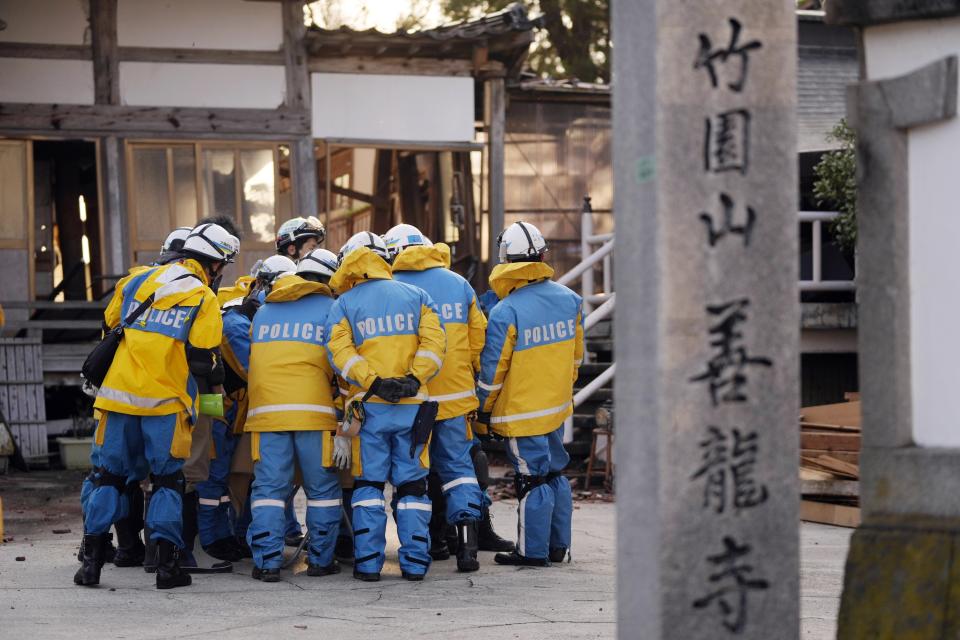 Police officers huddle up before getting into a building at the premises of a temple to search for victims in Wajima in the Noto peninsula, facing the Sea of Japan, northwest of Tokyo, Saturday, Jan. 6, 2024, following Monday's deadly earthquake. (AP Photo/Hiro Komae)