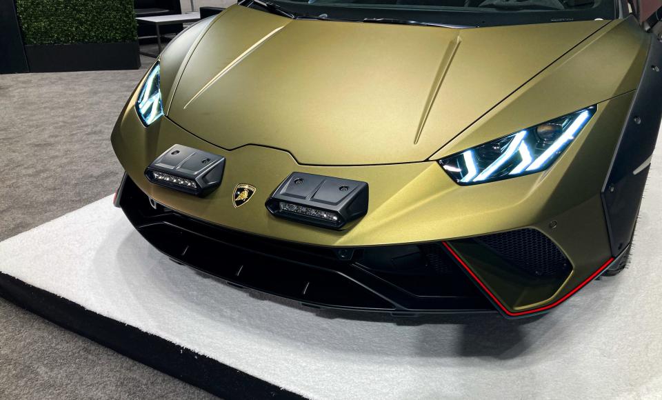 The nose of the shiny, green Lamborghini Huracan Sterrato, with V-shaped headlights illuminated.