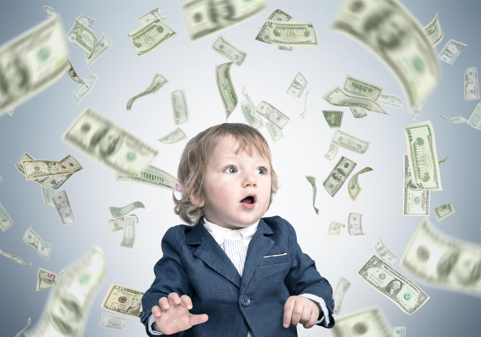 Portrait of a cute little baby boy wearing a suit and standing under a dollar rain against a gray wall. Concept of heritage.