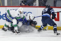 Winnipeg Jets' Evgeny Svechnikov (71) is checked by Vancouver Canucks' Oliver Ekman-Larsson (23) as Canucks' Jason Dickinson (18) and Jets' Jansen Harkins (12) go for the puck during first-period NHL hockey game action in Winnipeg, Manitoba, Thursday, Jan. 27, 2022. (John Woods/The Canadian Press via AP)