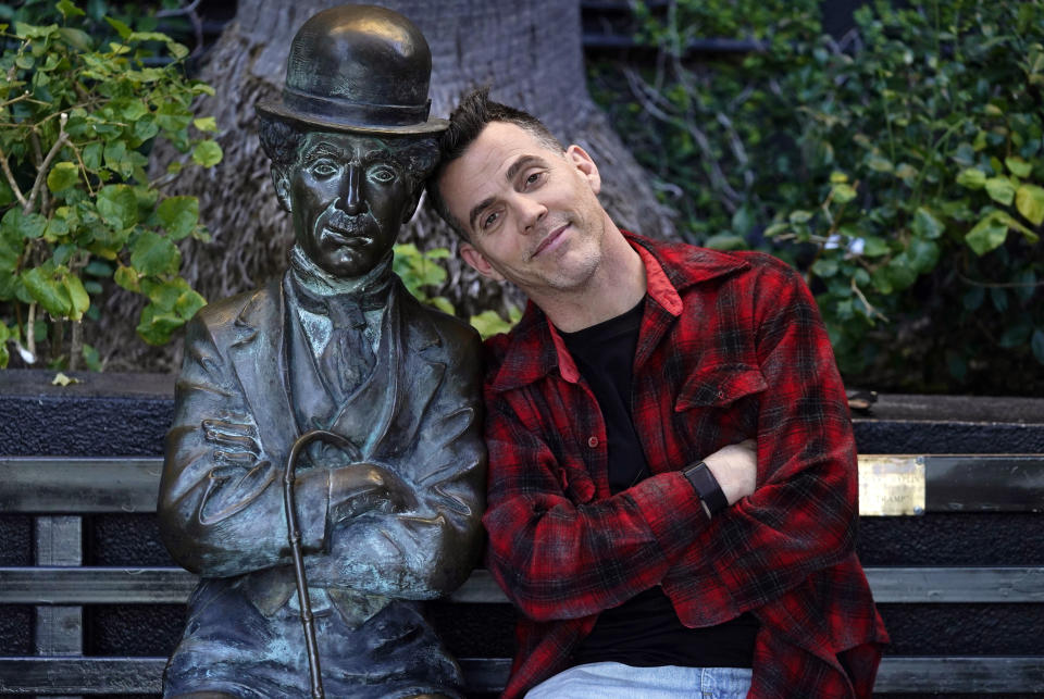 Steve-O, miembro del elenco de la película "Jackass Forever", posa junto a una estatua de Charlie Chaplin en un banco en The Hollywood Roosevelt, el jueves 27 de enero de 2022 en Los Ángeles. (AP Foto/Chris Pizzello)