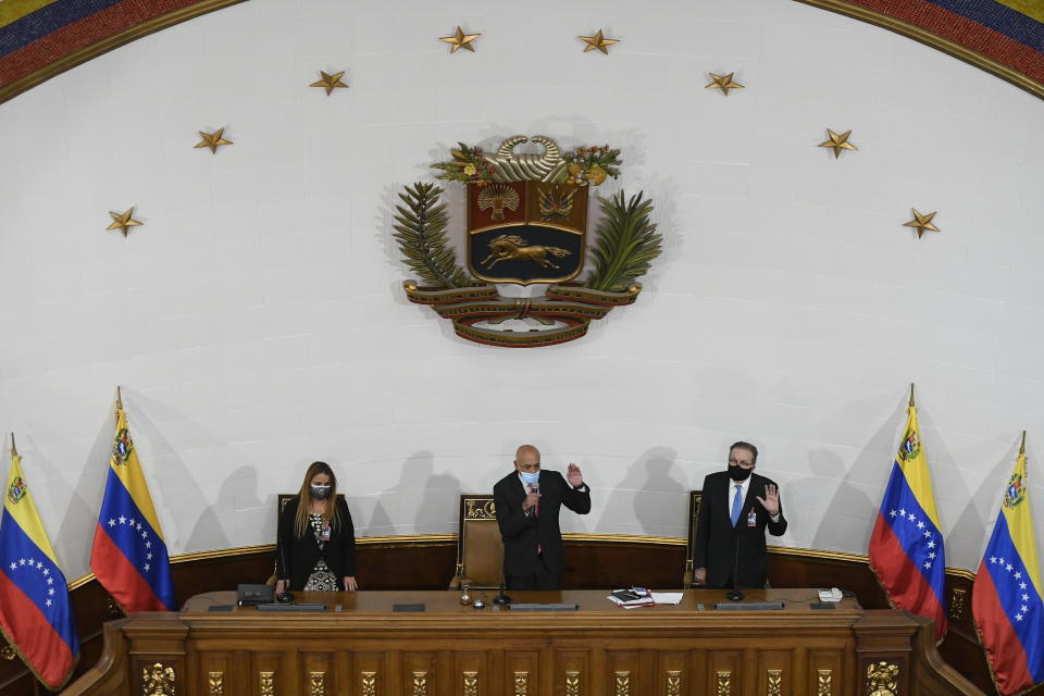 Jorge Rodriguez holds his hand up to swear-in lawmakers after he was sworn-in as president of the National Assembly in Caracas, Venezuela, Tuesday, Jan. 5, 2021, next to First Vice President of Congress Iris Varela, left, and Second Vice President Didalco Bolivar. The ruling socialist party assumed the leadership of Venezuela's congress, the last institution in the country it didn't already control. (AP Photo/Matias Delacroix)