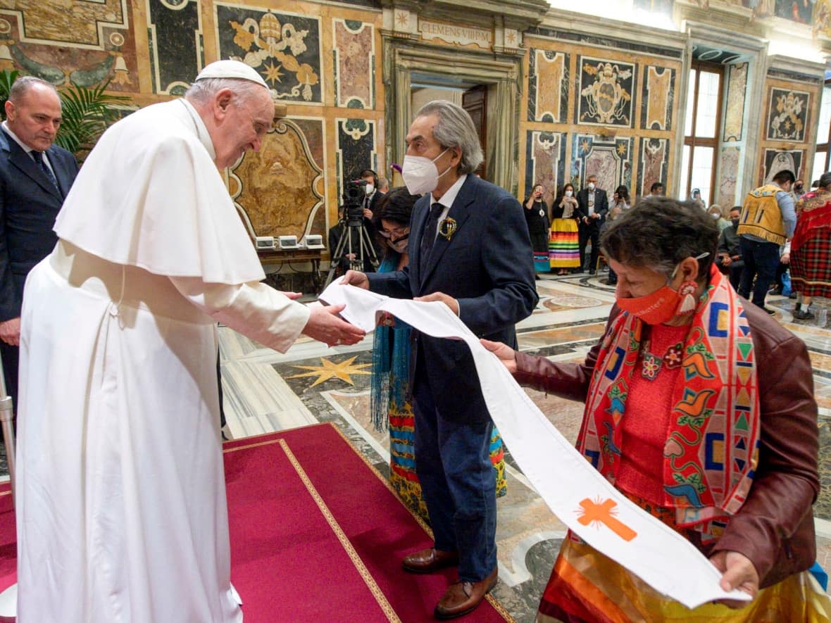 A beaded leather stole (liturgical vestment worn by a priest over the shoulders) is presented to the Holy Father by Linda Daniels (right) and former national chief of Canada's Assembly of First Nations Phil Fontaine (centre). The leather garment, beaded with orange crosses, was crafted by Therese Dettanikkeaze from the Northlands Denesuline Nation, Manitoba. (Vatican Media/Reuters - image credit)