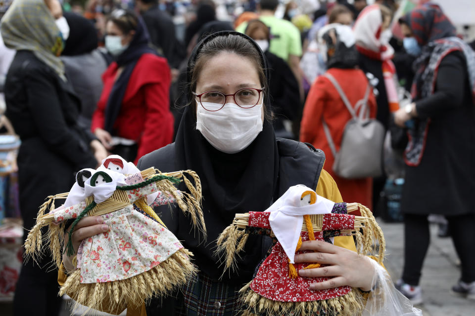 A vendor holds up hand crafted dolls made with wheat as she waits for customers ahead of the Persian New Year, or Nowruz, meaning "New Day." in northern Tajrish Square, Tehran, Iran, Monday, March 15, 2021. (AP Photo/Vahid Salemi)