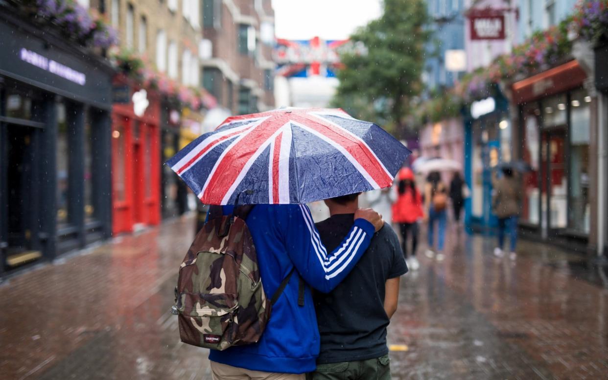 Tourists shelter from the rain in London under an umbrella featuring the Union Jack - © 2018 Bloomberg Finance LP