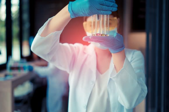 Laboratory worker holding four test tubes in front of their face.