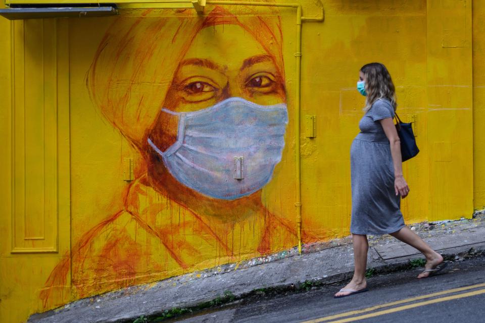 TOPSHOT - A pregnant woman wearing a face mask as a precautionary measure walks past a street mural in Hong Kong, on March 23, 2020, after the citys Chief Executive announced plans to temporarily ban the sale of alcohol in bars and restaurants as a measure to help stop the spread of the COVID-19 caused by the novel coronavirus. - Hong Kong will ban all non-residents from entering the city from midnight on March 24, 2020 in a bid to halt the coronavirus, its leader says, as she unveils plans to stop restaurants and bars serving alcohol. (Photo by ANTHONY WALLACE / AFP) (Photo by ANTHONY WALLACE/AFP via Getty Images)