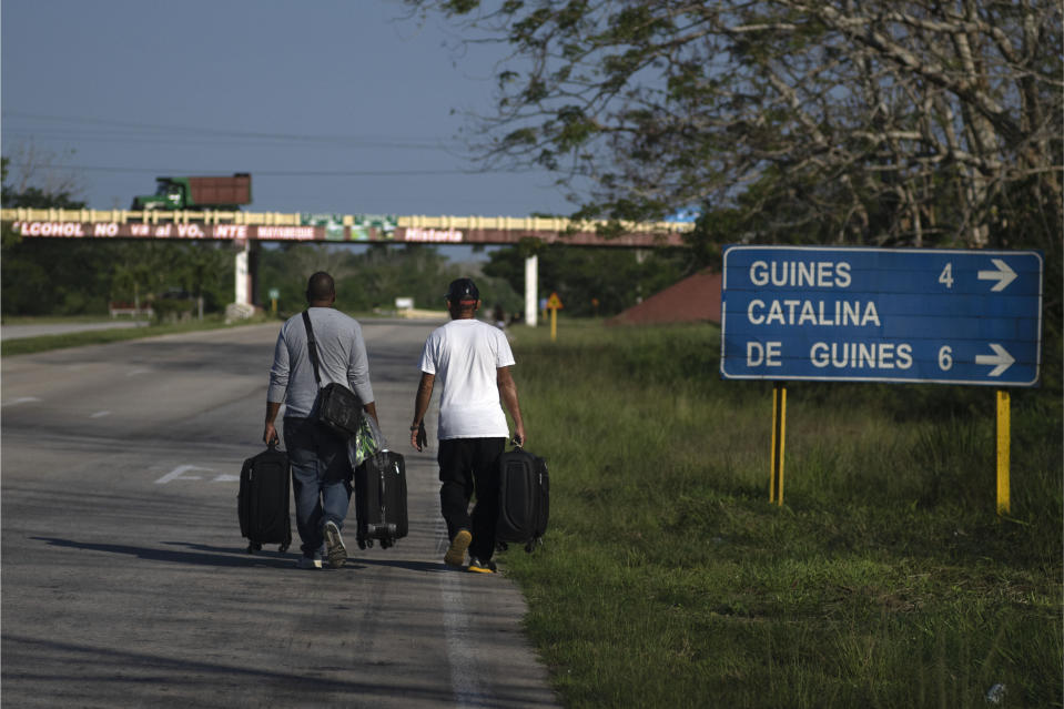 People with suitcases walk along a highway in search of a bus or taxi in Catalina de Guines, Cuba, Friday, May 19, 2023. Cuba has been restricting fuel sales amid a gas shortage. (AP Photo/Ramon Espinosa)