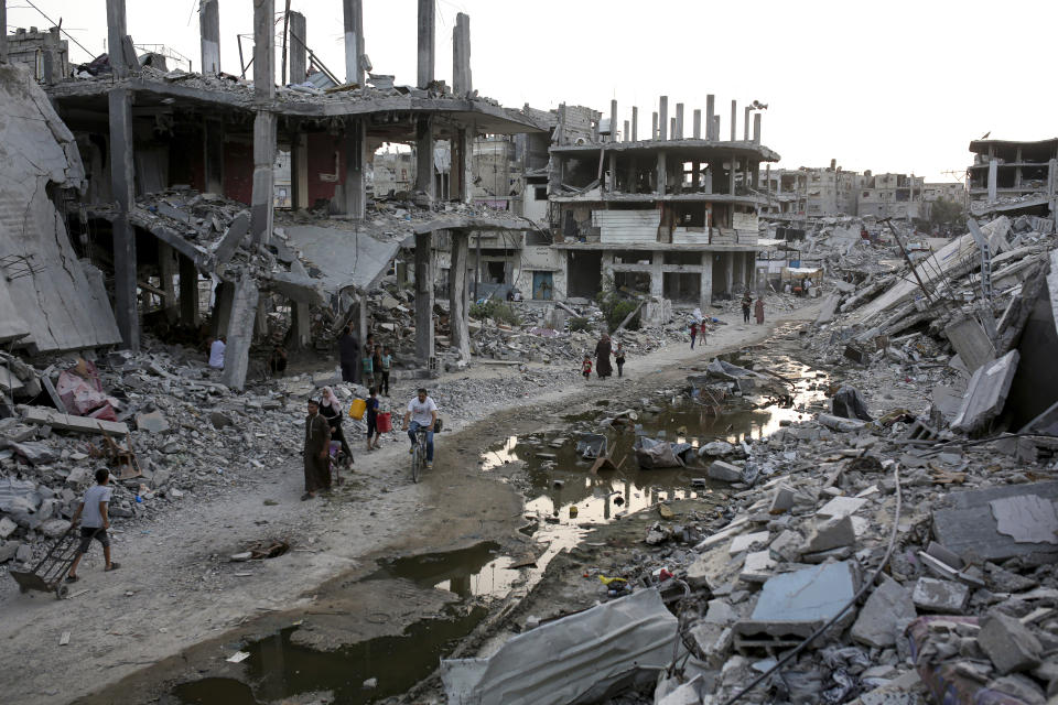 Palestinians displaced by the Israeli air and ground offensive on the Gaza Strip walk next to a dark streak of sewage flowing into the streets of the southern town of Khan Younis, Gaza Strip, Thursday, July 4, 2024. (AP Photo/Jehad Alshrafi)