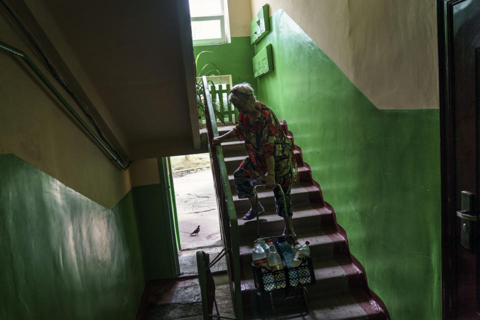 Lyubov Mahlii, 76, pulls a crate of water bottles up the stairs to her fifth floor apartment after filling them up at a nearby park in Sloviansk, Donetsk region, eastern Ukraine, Saturday, Aug. 6, 2022. Mahlii said that she doesn't have the money to relocate to a safer place, and that if she did, she wouldn't have anywhere to go. She hasn't made plans for what she'll do once cold weather arrives, but after 47 years in her apartment, she will face whatever comes from her home. "We are surviving!" she said. "We are surviving by any means." (AP Photo/David Goldman)