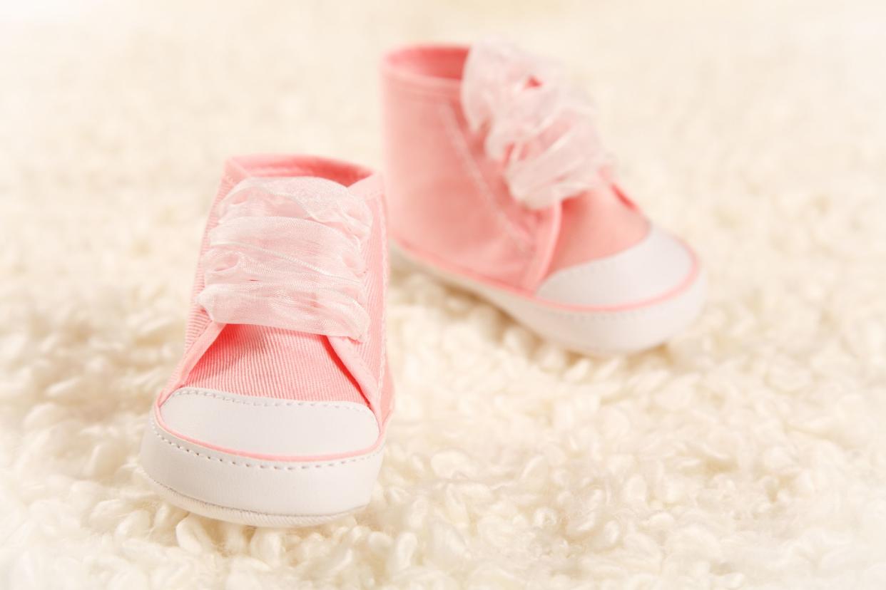 Closeup of a pair of pink baby sneakers with light pink ribbon laces on a very light pink mohair carpet