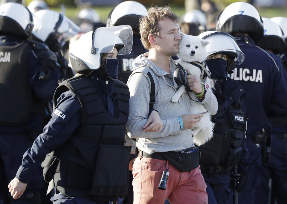 Police detain a man with a dog, in Warsaw, Poland, Saturday, Oct. 24, 2020. The man was among protesters angry at new restrictions aimed at fighting the coronavirus pandemic. The clashes come amid rising social tensions and as new restrictions just short of a full lockdown took effect Saturday.(AP Photo/Czarek Sokolowski)