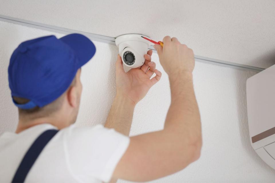 A man fixes a security camera on a ceiling with a tool.