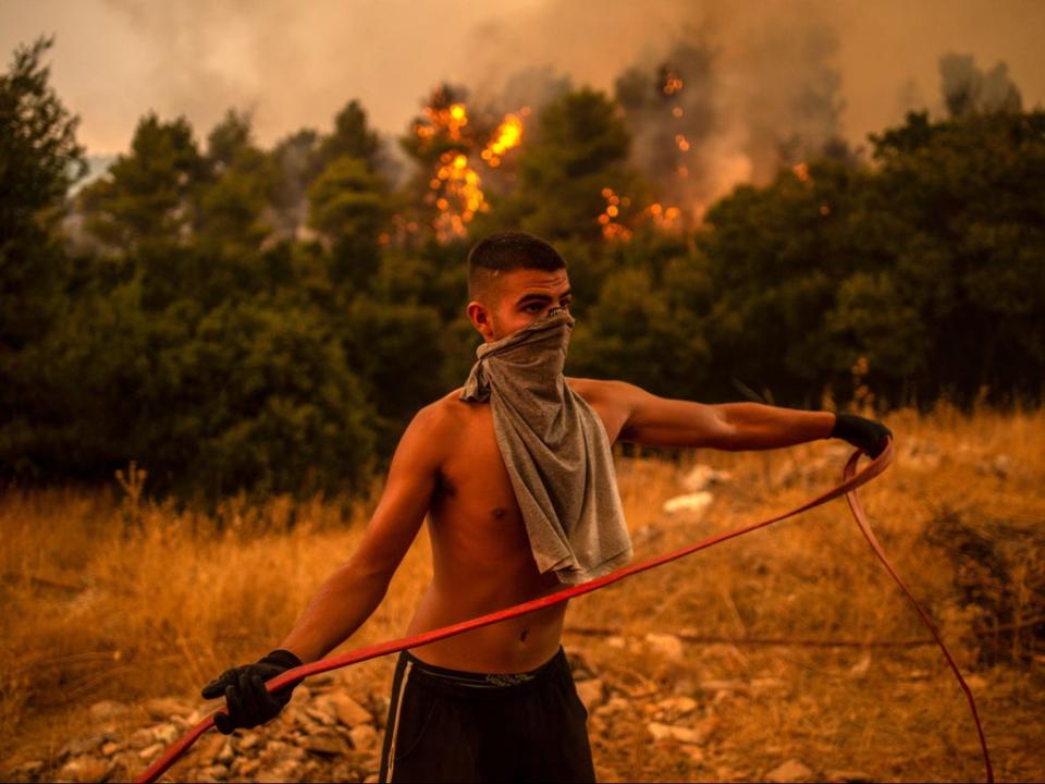 A volunteer holds a water hose during efforts to try to extinguish a fire in the village of Villa, north of Athens (AFP via Getty Images)