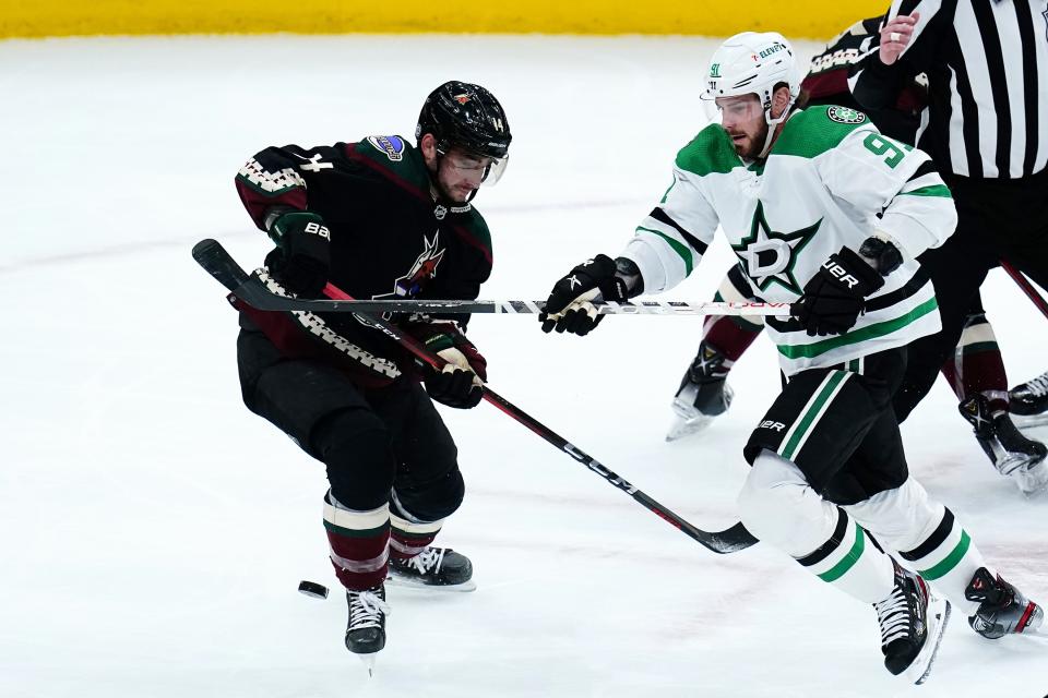 Dallas Stars center Tyler Seguin (91) battles with Arizona Coyotes defenseman Shayne Gostisbehere (14) for the puck during the first period of an NHL hockey game Sunday, Feb. 20, 2022, in Glendale, Ariz. (AP Photo/Ross D. Franklin)