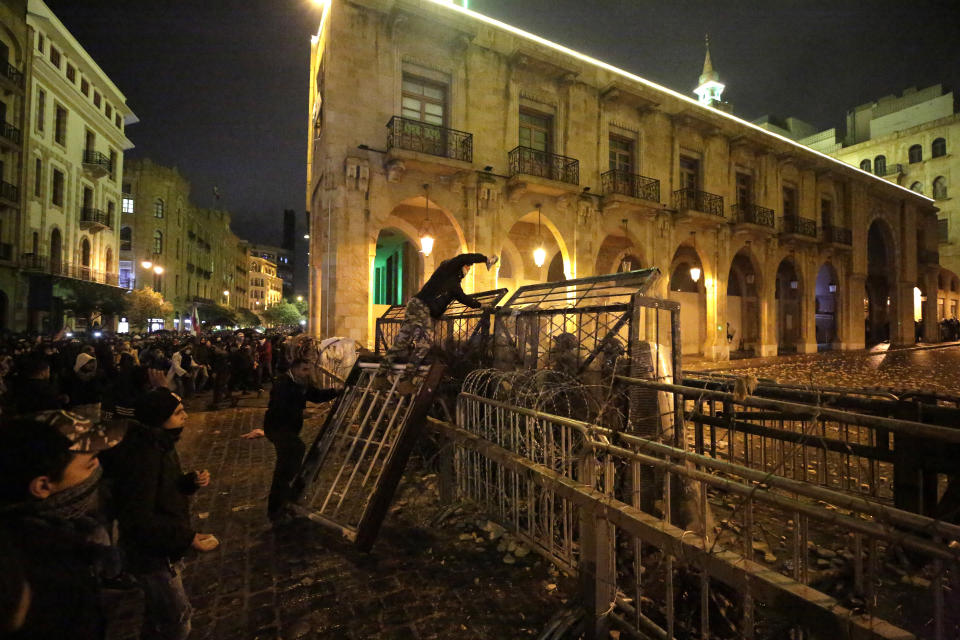 An anti-government protester stands on barriers as he throws stones against riot police during ongoing protests against the political elites who have ruled the country for decades, in Beirut, Lebanon, Sunday, Jan. 19, 2020. (AP Photo/Hassan Ammar)