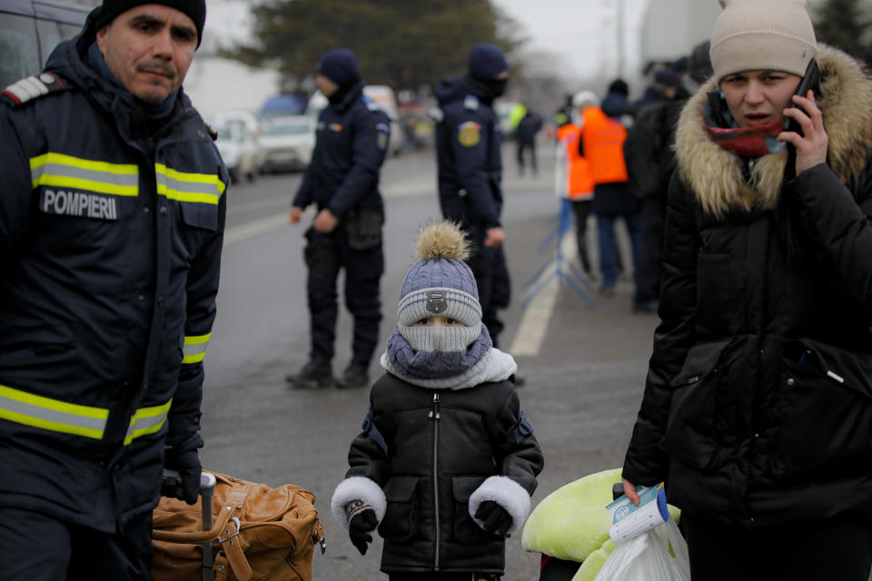 A firefighter helps refugees fleeing the conflict from neighbouring Ukraine at the Romanian-Ukrainian border, in Siret, Romania, Friday, March 4, 2022. The number of refugees who have fled Ukraine has now reached 1.2 million, the International Organization for Migration said Friday. This could become the "biggest refugee crisis this century," the U.N. has said, predicting that as many as 4 million people could leave. (AP Photo/Andreea Alexandru)