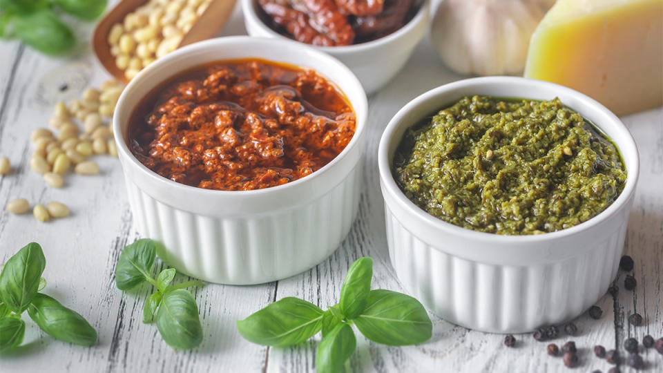 A ramekin of sun dried tomato pesto next to a ramekin of basil pesto