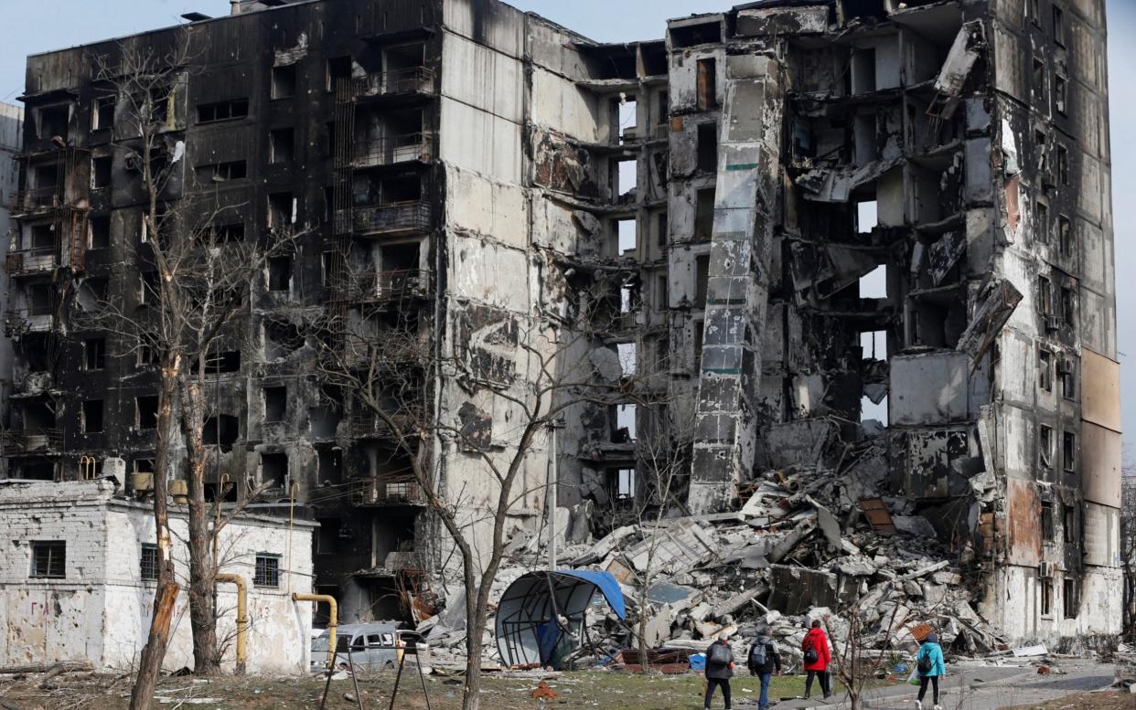 Mariupol residents walk near a destroyed apartment - ALEXANDER ERMOCHENKO /REUTERS