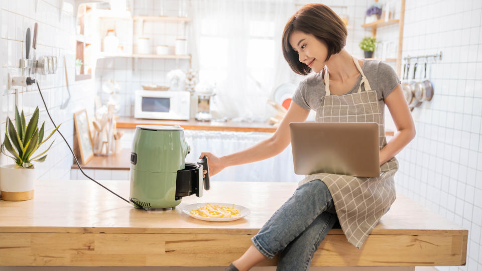 A woman opening an air fryer in a kitchen