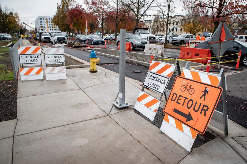 Signs redirect pedestrians and bikes at the corner of Pearl Street and East 8th Avenue in downtown Eugene where the city is widening sidewalks and adding protected bike lanes.