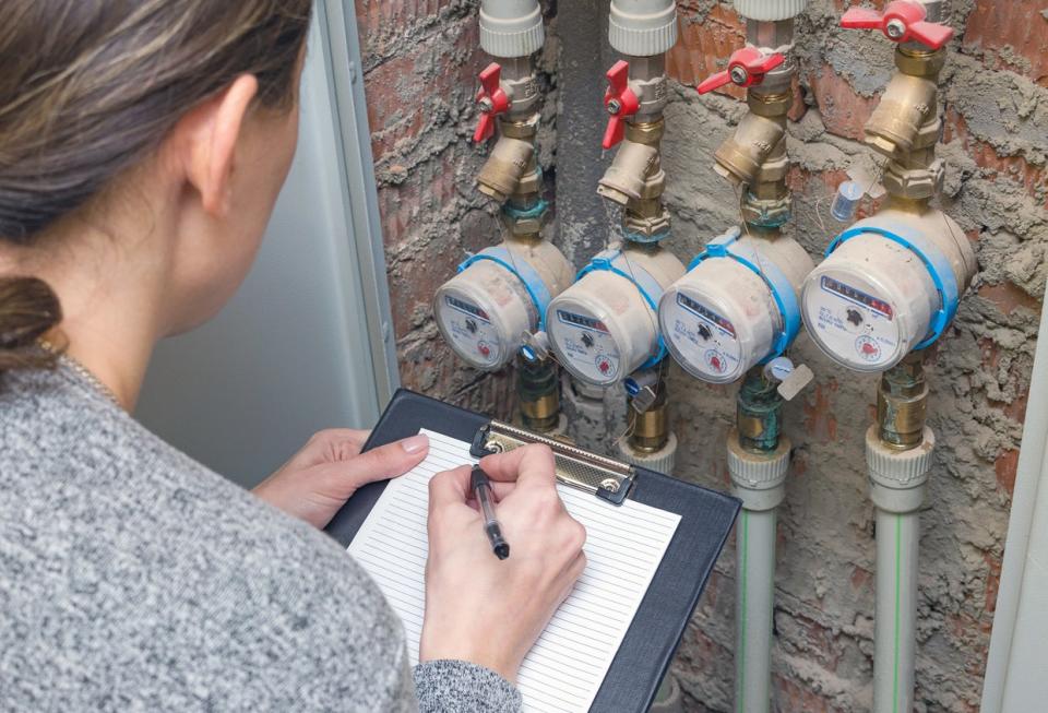 Woman with a clipboard and pen observing water meter readings.