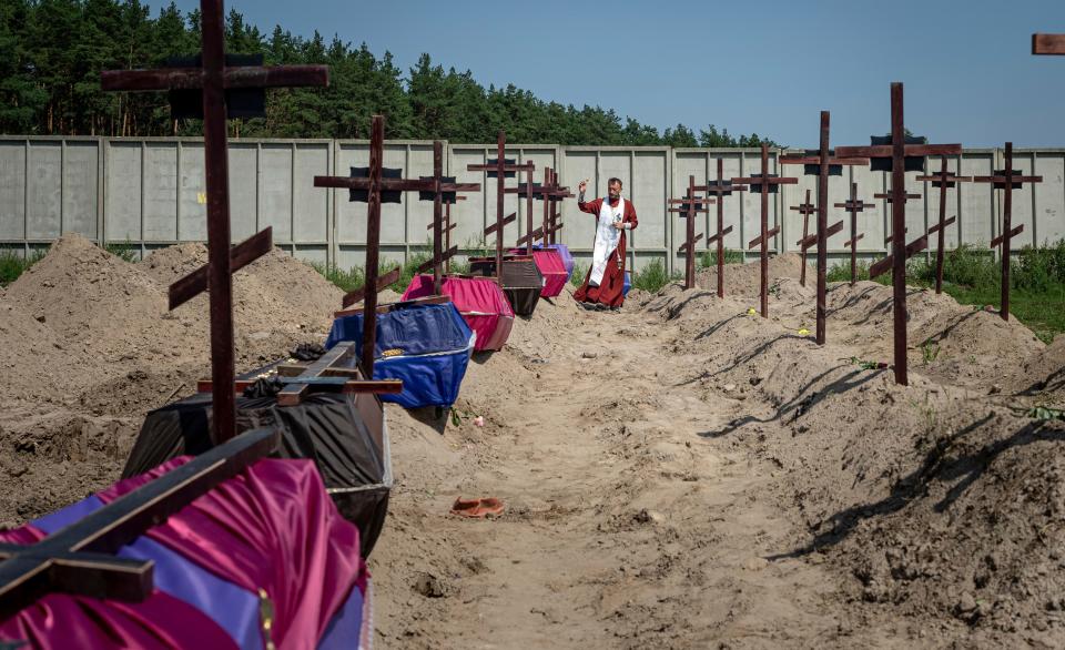 Orthodox priest Father Andriy blesses the coffins of unidentified civilians killed by Russian troops during Russian occupation in Bucha near Kyiv, Ukraine, on Wednesday, Aug. 17, 2022.