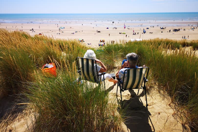 Two people sat on deckchairs at the back of beach looking towards the sea