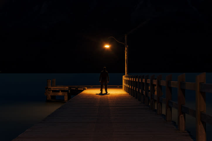 Person standing at the end of a pier under a streetlight at night